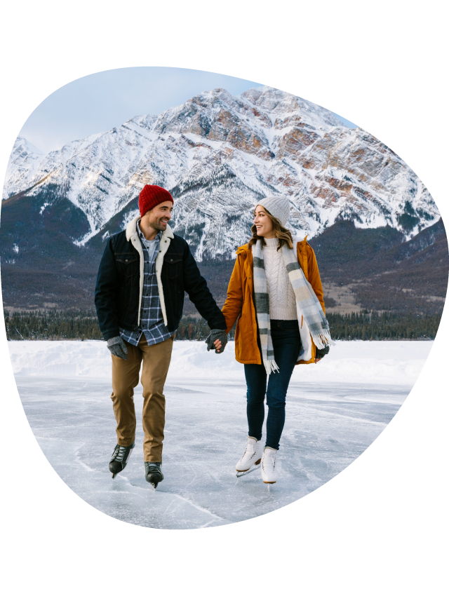 Two people hold hands, ice skating on a frozen lake.