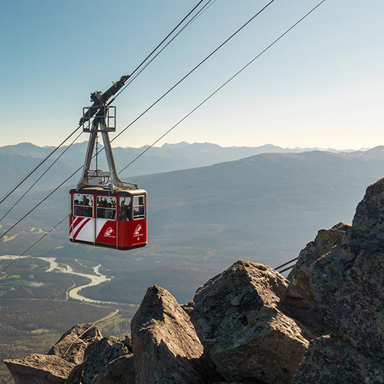 A red aerial tram ascends up a mountianside.