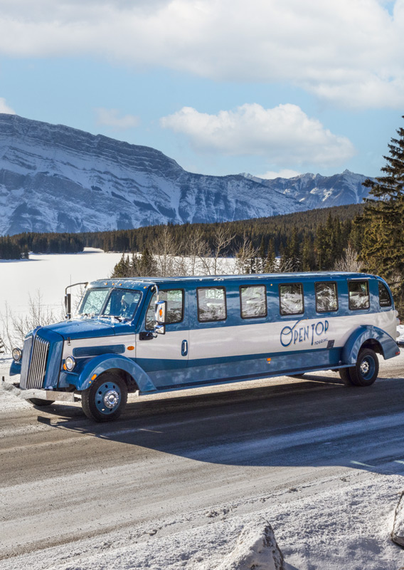 A historic style bus parked in front of a mountain view in the winter.