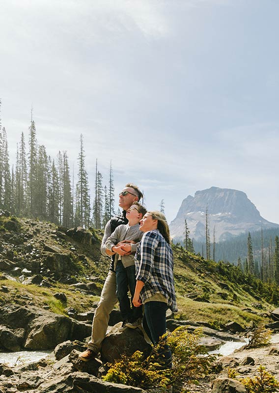 A young family stand on rocks outdoors and gaze upwards.
