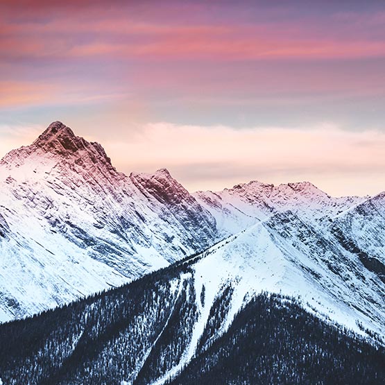 Snow-covered mountains below a pink sky.