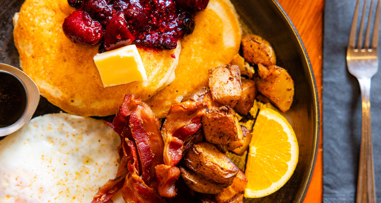 A top view of pancakes, bacon, eggs and roated potatoes set on a restaurant table.
