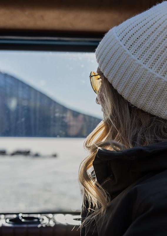A woman looks out from a vehicle window towards a snowy landscape.