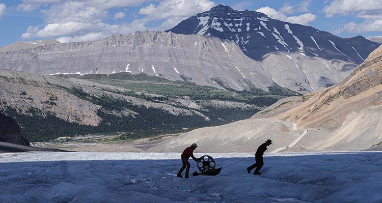 Two researchers pull their gear across the Glacier, a mountain in the background.