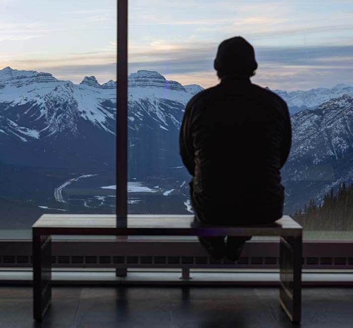 A person sits at a windowside bench looking at a mountain vista.