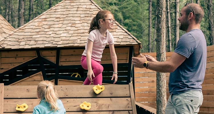 Father holds out his arms to his children climbing on a play area.