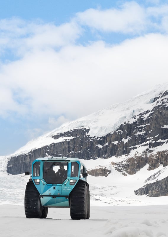 An Ice Odyssey vehicle drives on a glacier between two mountains.
