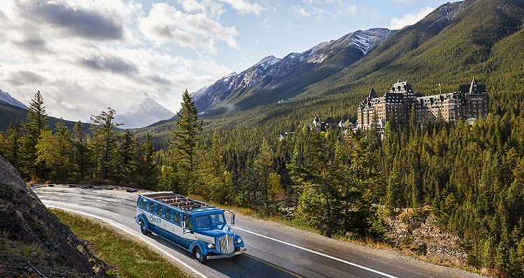 An Open Top Touring vehicle driving by a historic hotel in summer.