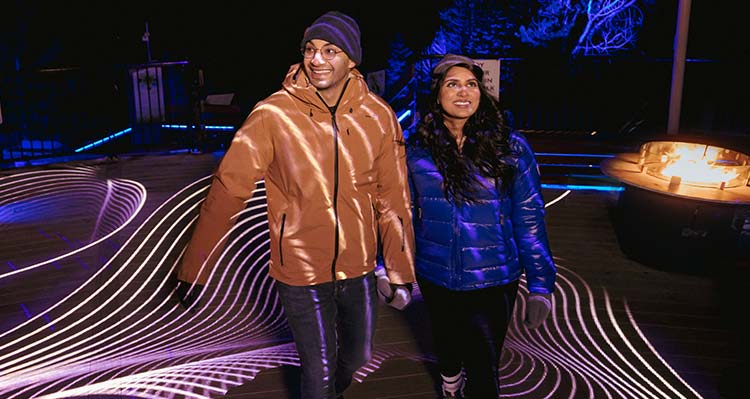A man and woman walk through Nightrise, with a wave pattern light covering them.