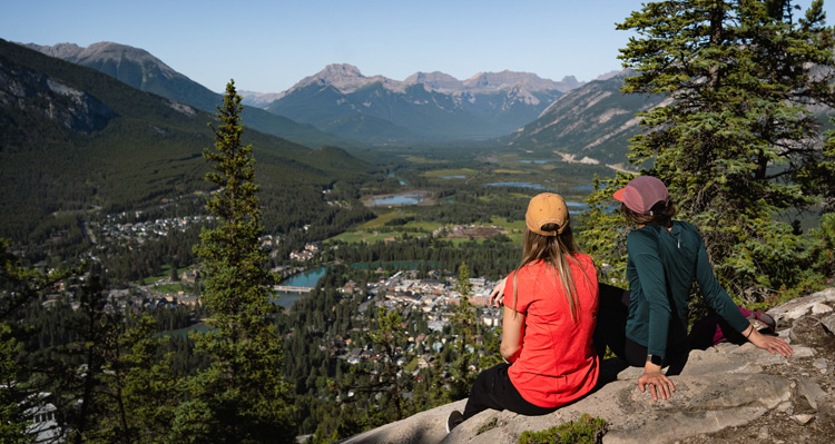 Two people sitting at a viewpoint looking at the town below