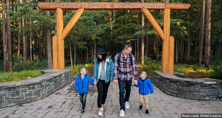 A family walks down a pathway below a wooden sign for Johnston Canyon.
