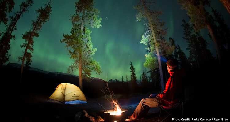 A person sitting by a campfire looking at the Northern Lights